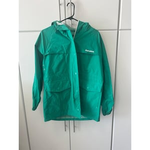 May include: A bright green hooded raincoat with the word "Rainskins" printed on the chest. The jacket has a button-up front, two large front pockets, and a drawstring hood. The jacket is hanging on a black hanger.