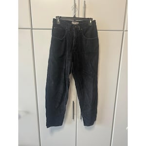 Pode incluir: Uma calça de veludo cotelê cinza chumbo escuro com textura de listras verticais, fecho de botão e zíper, cinco bolsos e uma etiqueta da marca no cós traseiro. A calça está pendurada em um cabide de plástico preto.