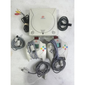 Peut inclure: Console Dreamcast crème avec deux manettes assorties, des câbles et des connecteurs. Les manettes ont des boutons colorés et de petits écrans. La console porte le logo Dreamcast sur le dessus.