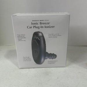 May include: A white product box for a Sharper Image Design Ionic Breeze Car Plug-In Ionizer. The box features a black, oval-shaped car air ionizer with an articulated plug, along with printed text describing its features and operation.