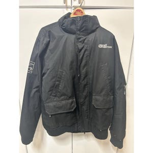 May include: Black jacket with a high collar, two large front pockets, and a ribbed hem. The jacket has the text "GEKO FUNCTION" printed on the chest and "ICI" on the left sleeve. The jacket is made of a durable, water-resistant material.
