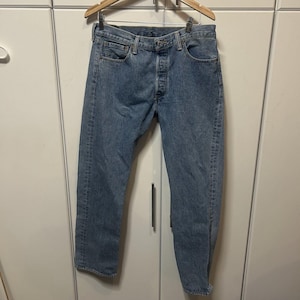 May include: A pair of light blue denim jeans featuring a classic five-pocket design, a button fly closure, belt loops at the waistband, and copper-toned metal rivets at the pocket corners, presented in a straight-leg cut with a medium wash finish.