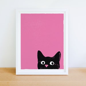 Cute and funny black cat art print with a bubblegum pink background and a black cat head peeking up over the bottom right edge of the print. The cat's eyes are open wide like it is surprised or excited and it has a pink nose.