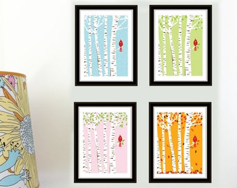 May include: Four framed art prints featuring birch trees and red birds against backgrounds of blue, green, pink, and orange, representing the seasons. The prints are displayed on a white wall. A vintage timer and colorful blocks are in the foreground.