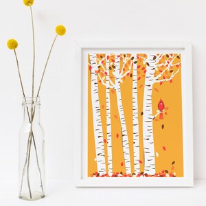 May include: A white framed print of a stylised illustration of a birch tree forest with a red cardinal perched on a branch. The background is a solid yellow colour with red and brown leaves falling from the trees.