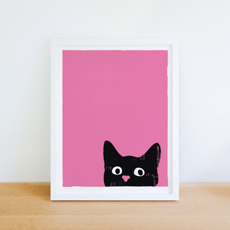 Cute and funny black cat art print with a bubblegum pink background and a black cat head peeking up over the bottom right edge of the print. The cat's eyes are open wide like it is surprised or excited and it has a pink nose.