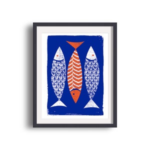 May include: A framed art print featuring three stylized fish against a blue background. Two fish are white with detailed scale patterns, flanking a central orange fish with vertical stripes. The artwork is in a black frame.