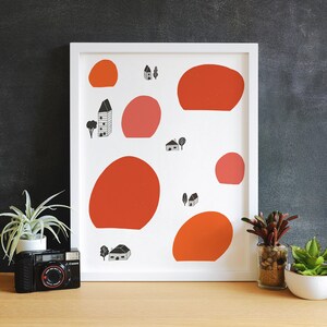 May include: A white framed print with a minimalist design featuring red and pink circles, small houses, and trees. The print has a white background and black outlines.