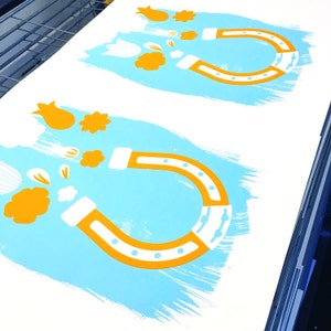 May include: Two white horseshoe magnets with orange outlines on a light blue background. The magnets are attracting small white and orange flowers.