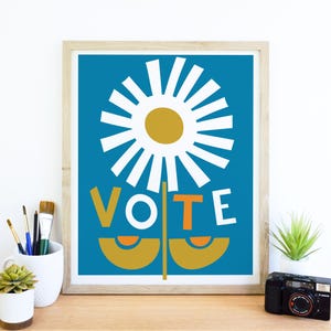 May include: A blue and white print with a stylized daisy and the word "VOTE" in bold, orange, white, and yellow letters. The daisy has a yellow center and white petals. The stem is a stylized green shape with two yellow circles.
