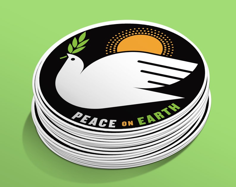 May include: A stack of round stickers with a black and white design. The sticker features a white dove with an olive branch in its beak, a yellow sun, and the text "Peace on Earth".