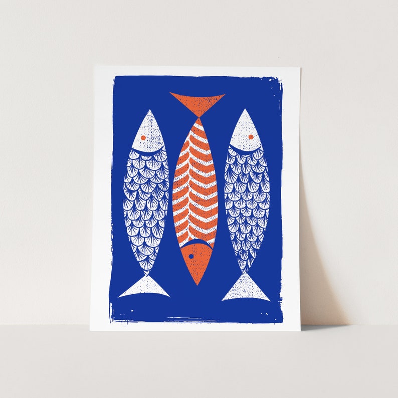 May include: A blue and white print featuring three stylized fish. Two fish are white with blue scale patterns, and the central fish is orange with a striped design. The fish have orange eyes and tails, set against a deep blue background.