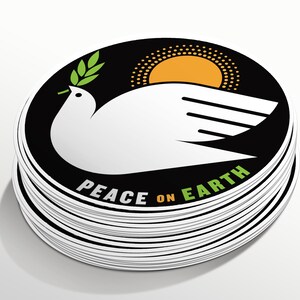May include: A stack of round stickers with a black background, a white dove with an olive branch in its beak, a yellow sun, and the text "Peace on Earth".