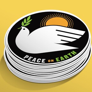 May include: A stack of round stickers with a black background and a white dove holding a green olive branch. The dove is flying over a yellow sun with a black dotted outline. The text "Peace on Earth" is written in green and white on the sticker.