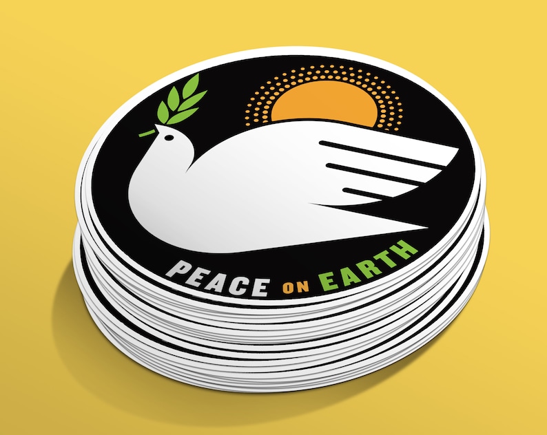 May include: A stack of round stickers with a black background and a white dove holding a green olive branch. The dove is flying over a yellow sun with a black dotted outline. The text "Peace on Earth" is written in green and white on the sticker.