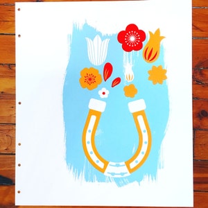 May include: A blue and white horseshoe magnet with red, orange, and white flowers and petals around it.