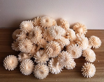 May include: A pile of cream-coloured, wooden, decorative flowers. The flowers are arranged in a loose, organic pattern.