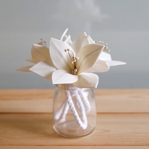 May include: White wooden flowers in a clear glass vase with white rope diffusers.