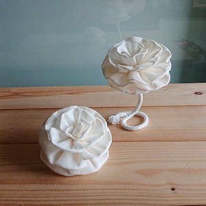 Puede incluir: Dos difusores de flores de madera de sola blanca sobre una superficie de madera. La flor de la izquierda está tumbada, mientras que la flor de la derecha está de pie con una cuerda blanca atada a la parte inferior.