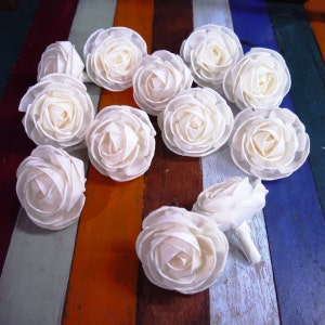 May include: A collection of 12 white sola wood flower rosettes arranged in a heart shape on a colorful wooden background.