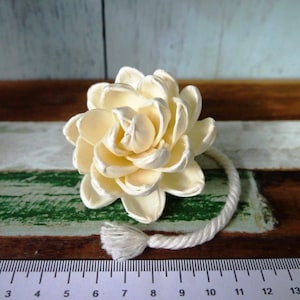 Op de afbeelding: Een witte sola-houten bloem met een touw eraan bevestigd. De bloem heeft een diameter van ongeveer 5 cm.