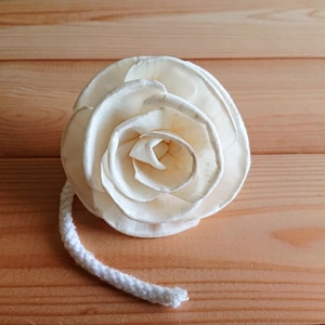 May include: A white wooden rose with a rope attached to the bottom. The rose is made of multiple layers of wood, creating a realistic flower shape.