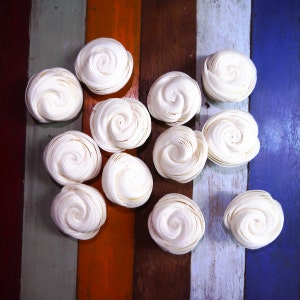 May include: A collection of 11 white paper roses arranged on a colorful wooden surface. The roses are made of paper and have a delicate, ruffled texture.