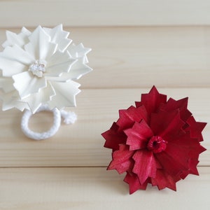 Puede incluir: Dos flores de papel, una blanca y otra roja, se muestran sobre una superficie de madera. La flor blanca tiene un pequeño botón blanco en el centro. La flor roja tiene un pequeño botón rojo en el centro.