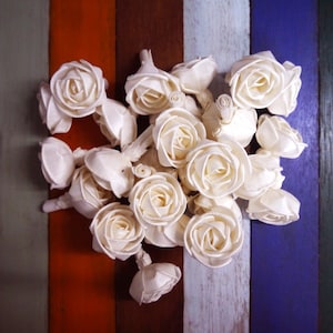 Può includere: Un bouquet di fiori di legno bianco a forma di rosa disposti su uno sfondo di legno colorato.