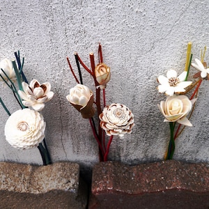May include: A bouquet of white wooden flowers with different shapes and textures. The flowers are arranged in three separate bouquets and are placed on a gray concrete surface.