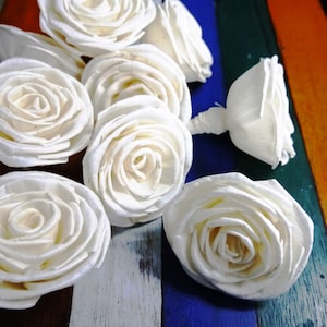 May include: A group of white, paper, rose-shaped decorations. The roses are arranged on a colourful striped surface.