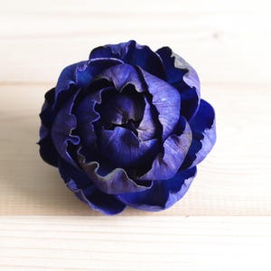 May include: A single, deep blue, fabric flower resembling a peony. The flower is made of layered petals and has a slightly textured surface.