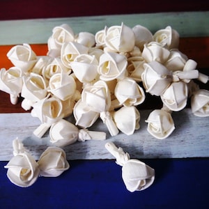 May include: A pile of white wooden rose flower buds, arranged on a colorful striped surface. The flowers are made of wood and have a natural, rustic look.