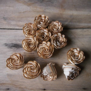 May include: A collection of 12 wooden roses in a light brown color. The roses are arranged in a circle on a wooden surface.