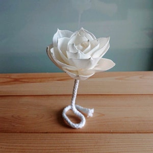 May include: A white wooden rose with a white rope stem. The rose is on a wooden surface.