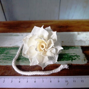 May include: A white sola wood flower with a rope tied around it. The flower is on a wooden surface with a ruler in the foreground.