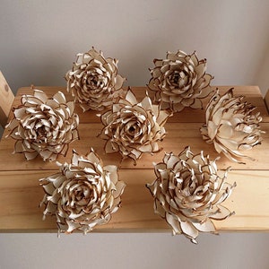 Puede incluir: Siete rosetas de flores de madera de sola de color crema con bordes marrones. Las rosetas están dispuestas sobre una superficie de madera.