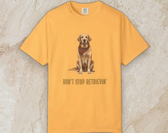 May include: A golden yellow short-sleeved t-shirt featuring a centered illustration of a golden retriever dog wearing a dark red bandana. Below the dog, the text "DON'T STOP RETRIEVIN'" is printed in a simple, dark brown sans-serif font.