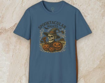 May include: A slate blue short-sleeve t-shirt featuring a graphic print of a skull wearing a witch hat and holding a golf club. The design includes three orange jack-o'-lanterns, bats, and the text SPOOKTACULAR NIGHTS in a dark brown font.