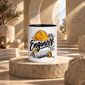 Pode incluir: Uma caneca de cerâmica branca com borda preta apresentando um gráfico de um capacete amarelo, uma engrenagem, uma planta enrolada, um triângulo, uma caneta e uma fita métrica. O texto diz Engineer, Problem Solver, Builder, Innovator.