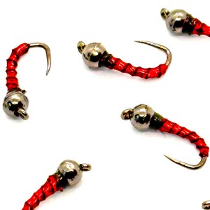 Op de afbeelding: Close-up van verschillende vliegvisvliegen. Elke vlieg heeft een zilveren kraalkop, een rode body met zwarte strepen en een gebogen haak. De vliegen zijn ontworpen om mee te vliegvissen.