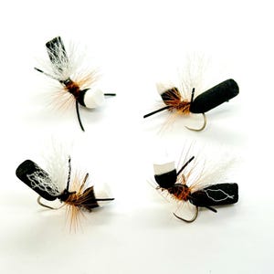 May include: Four black and white fly fishing lures with white foam heads and black foam bodies. The lures have brown and white feathers.