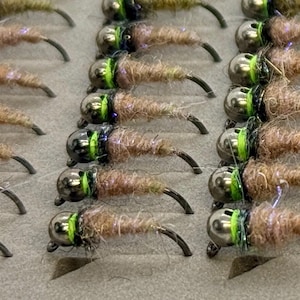 May include: Close-up of several fishing flies. Each fly has a silver-colored head, a brown body, and a curved black hook. The flies are arranged in neat rows, suggesting they are stored in a fly box or similar container.