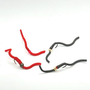 Op de afbeelding: Drie vliegenvisserlokken, twee rood en één zwart, met gouden kralen. De lokken zijn gemaakt van zacht, flexibel materiaal en zijn ontworpen om wormen of larven na te bootsen.