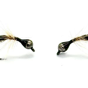 May include: Two black and silver fly fishing flies with white feathers.