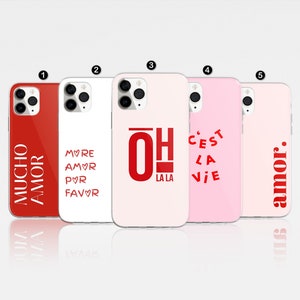 May include: Five different phone cases with various designs. The cases are all pink and white with red text. The designs include "Mucho Amor", "More Amor Pvr Favor", "Oh La La", "C'est La Vie", and "Amor."