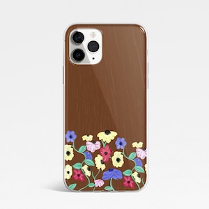 May include: A clear phone case with a brown wood grain effect. The bottom of the case features a colourful floral pattern with yellow, pink, blue, and white flowers. The case has a clear border.