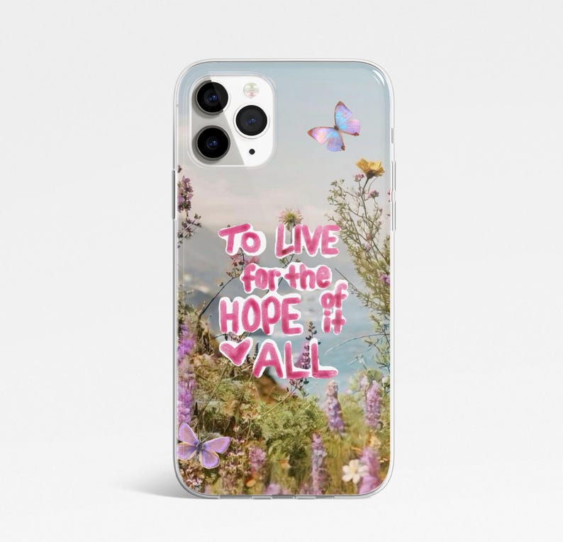 May include: Transparent phone case with a floral and butterfly design. The case has the text "To live for the hope of it all" in pink. The background shows a landscape with flowers and butterflies.