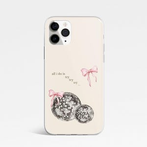 May include: A phone case with a pale beige background. It features two disco balls, pink bows, and the text "all I do is try try try...". The case is designed for a smartphone and has a clear, protective border.