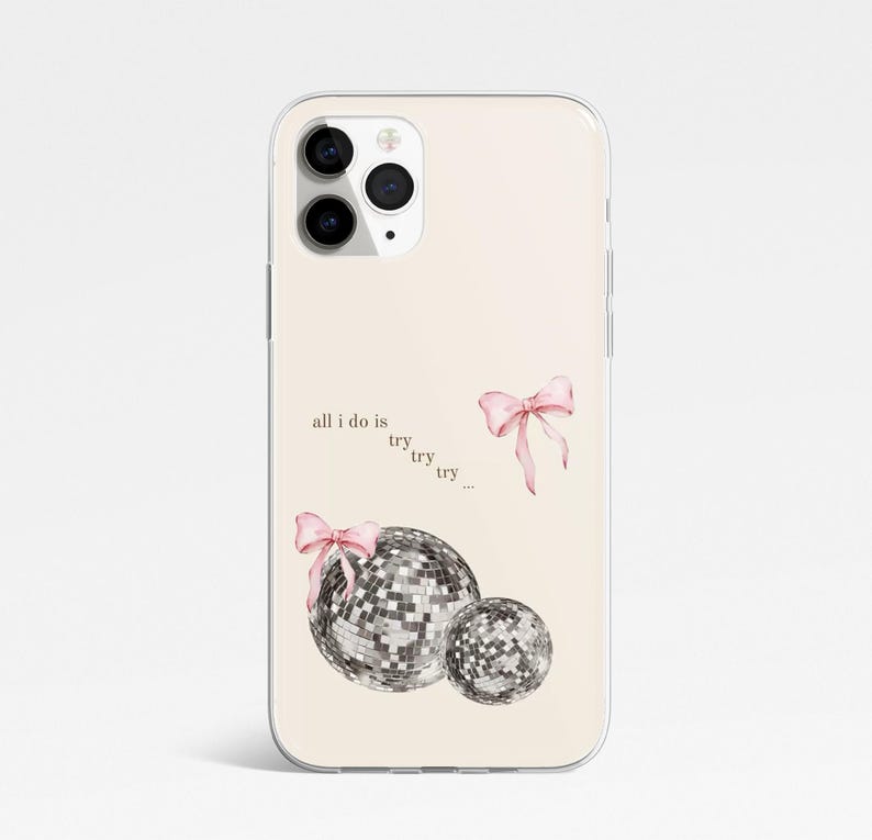 May include: A phone case with a pale beige background. It features two disco balls, pink bows, and the text "all I do is try try try...". The case is designed for a smartphone and has a clear, protective border.